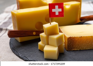 Swiss Cheeses, Block Of Medium-hard Yellow Cheese Emmental Or Emmentaler With Round Holes And Matured Gruyere Close Up Served In Cubes As Mountain Top With Swiss Flag.