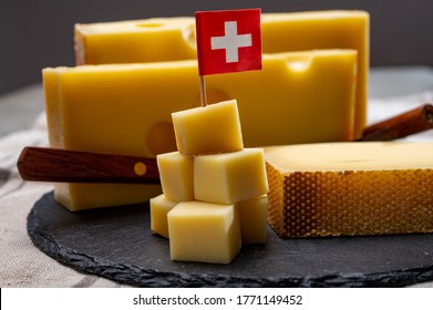 Swiss Cheeses, Block Of Medium-hard Yellow Cheese Emmental Or Emmentaler With Round Holes And Matured Gruyere Close Up Served In Cubes As Mountain Top With Swiss Flag.