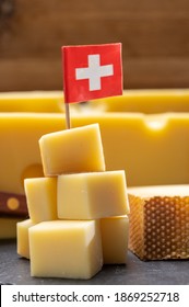 Swiss Cheeses, Block Of Medium-hard Yellow Cheese Emmental Or Emmentaler With Round Holes And Matured Gruyere Close Up Served In Cubes As Mountain Top With Swiss Flag.