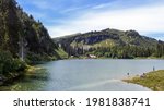 Swiss countryside. View of people fishing on the lake in the swiss alps surrounded by pines and rocky mountains in summer. Lac des Chavonnes, Canton Vaud, Switzerland