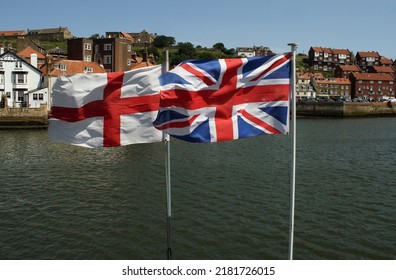 Swiss Flag And English Flag Waving Together Against A Water Background And Old English Buildings