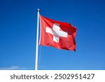 
Swiss flag flying in the wind blue sky, copyspace. swiss flag in the wind in front of a blue sky sunshine during the day. light veil clouds. direct democracy and freedom. sunshine during the day 