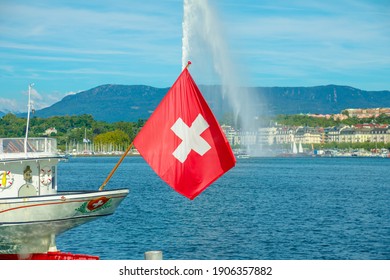 Swiss Flag in foregound and Jet d'eau fountain in Geneva Lake on background, the most famous attraction and symbol of the city. French Swiss in Switzerland.