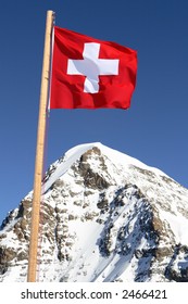 The Swiss Flag On A Background Of Beautiful Mountain Peaks