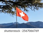 Swiss flag waving atop Monte Bre with mountains in the background, Lugano, Switzerland