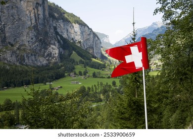 Swiss flag waving in front of a scenic alpine valley in Lauterbrunnen, Switzerland. The view features towering cliffs, lush green meadows, and mountain chalets, capturing the beauty of the Swiss count - Powered by Shutterstock