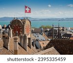 The Swiss flag waving at the top of the Clock Tower (Tour Diesse) in Neuchâtel. Panoramic view with rooftops, chimneys and the lake in the background in a sunny day