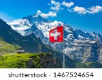 Swiss flag waving and tourists admire the peaks of Monch and Jungfrau mountains on a Mannlichen viewpoint, Bernese Oberland Switzerland