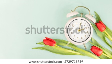Switch to daylight saving time in spring, summer time changeover, alarm clock with red tulip flowers