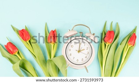 Switch to daylight saving time in spring, summertime changeover, alarm clock with red tulip flowers