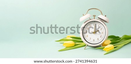 Switch to daylight saving time in spring, summer time changeover, alarm clock with yellow tulip flowers