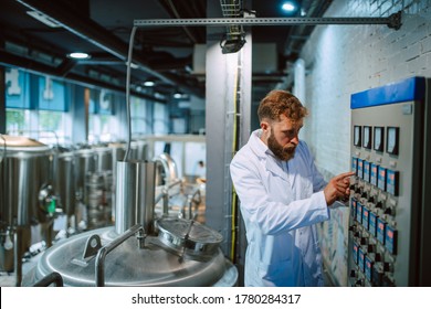 Switchboard Operator Controlling Machine In Production Plant. Caucasian Technologist Specialist In White Protective Suit Working In Food And Beverage Factory.