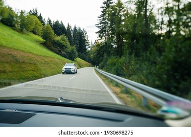 Switzerland - Sep 22, 2018: Driver POV At Car View At The Front Driving Mercedes-Benz SUV Electric Car - Driving On Rural Highway Surrounded By Tall Fir Trees - Tilt-shift Photo