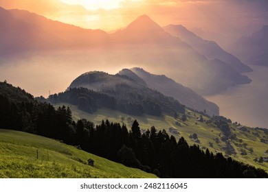 Ennetbürgen, Switzerland, taken at sunset. The soft, golden light casts a warm glow over the rolling hills, lush greenery, and misty mountains, creating a serene and picturesque scene. - Powered by Shutterstock