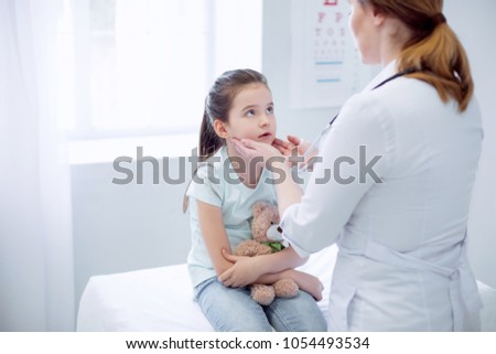 Swollen tonsils. Young pensive girl sitting while looking at female doctor who testing her tonsils
