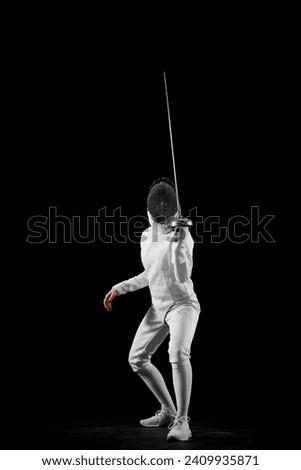 Swordswoman, professional female fencer's poised stance, against black studio background. Intensity and excitement of fencing. Concept of professional sport, active and healthy lifestyle, championship