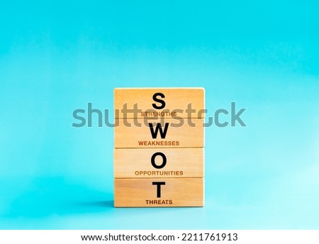 SWOT analysis concept. Four elements with text, Strengths, Weaknesses, Opportunities, Threats on wooden block stack on blue background. Planning technique operations and help develop strategic goals.