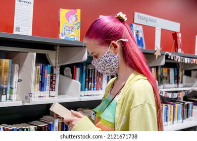 Sydney, Australia, 2022-01-25 Teenage Girl With Ombre Pink Purple Colored Hair Wearing Face Mask Choosing Books At The Local Library During The COVID-19 Pandemic.