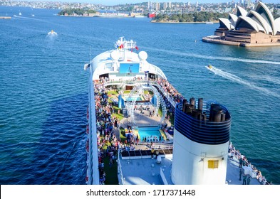 Sydney / Australia 22.Dec 2013: Cruise Ship With Lots Of People On Board, View From The Top. The Ship Leaves Port. Photo Of The Sydney Harbor Bridge, A Distant View Of The Sydney Opera House