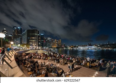 Sydney, Australia - April 15, 2017: Many tourists from over the world enjoy their time in Opera House, multi-venue performing arts centre in Sydney by night with financial towers in background.