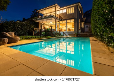 Sydney, Australia - August 1 2019: Suburban Domestic Two Story Home Lit Up At Night Viewed From Back Yard Next To Pool With Day Bed Or Lounge - Low Angle