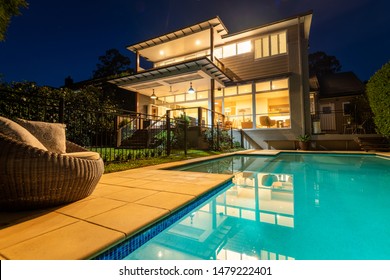 Sydney, Australia - August 1 2019: Suburban Domestic Two Story Home Lit Up At Night Viewed From Back Yard Next To Pool With Day Bed Or Lounge