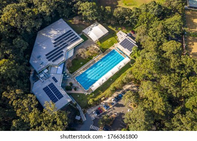 Sydney, Australia: Jun 26 2020: Aerial Shot Of An Outdoor Olympic Size, Six Lane, Swimming Pool At An Exercise Gym Complex Surrounded By Trees And Park In Afternoon Light, With People Swimming Laps