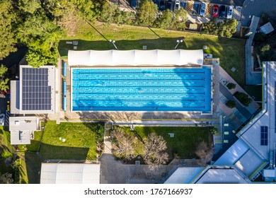 Sydney, Australia: Jun 26 2020: Overhead Aerial Shot Of An Outdoor Olympic Size, Six Lane, Swimming Pool In Afternoon Light, With People Swimming Laps