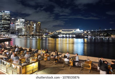 SYDNEY, AUSTRALIA - MARCH 7, 2018 - Friends And Tourists Enjoying The Lively Sydney Nightlife In Front Of A Cruise Ship Anchored In Circular Quay