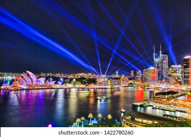 Sydney city CBD waterfront of Circular quay with high-rise buildings painted by light and blue laser beams in dark night sky during Vivid Sydney light show.