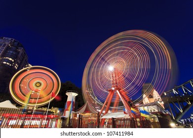 Sydney city luna park illuminated at sunset with blurred moving attractions wheels