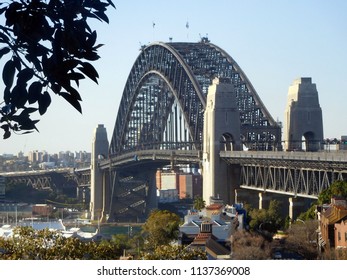 Sydney Harbour Bridge From Observatory Hill Looking North In Mid-afternoon Of Sunny Winter Day With Leaves Of Moreton Bay Fig Tree In Top Left Foreground