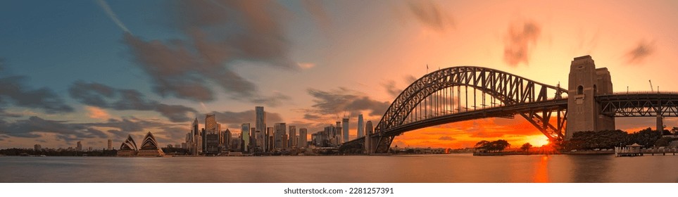 Sydney Harbour Bridge, Opera House and skyscrapers in the city are shrouded in pink afterglow under the reflection of the setting sun.