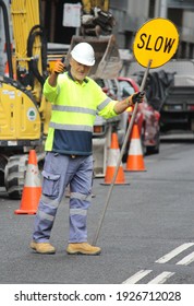 Sydney, NSW  Australia - February 25 2021: Male Traffic Controller Holding Yellow Slow  Lollipop Sign Directing Cars On The Road