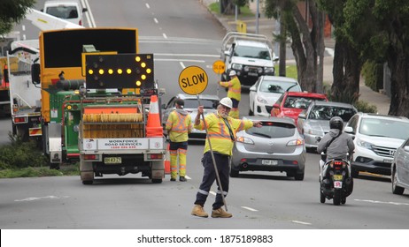 Sydney, NSW  Australia - July 14 2020:  Traffic Management. Man Directing Traffic Round Large Machinery On The Road That Is Cutting Down Street Trees.