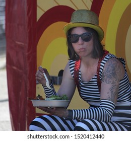 Sydney, NSW Australia - September 15 2019: Local Suburban Street Fair. Street Performer In Costume Sitting On A Milk Crate Eating Lunch. She Is Chewing Her Food.