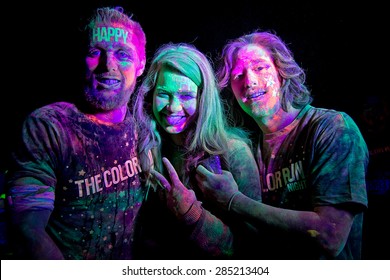 SYDNEY,AUSTRALIA - JUNE 6,2015: Three adults in the Color Run Night 5K fun run. Runners encounter bubble blowers, coloured powder and UV light, joining a dance party at the finish.
