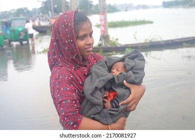 Sylhet, Bangladesh - 20 June 2022: Flood-hit Sylhet. A Woman Walks To A Safe Haven On A Flooded Road With Her Baby In Her Arms.