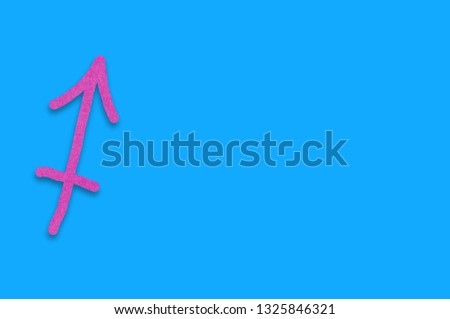 Symbol of astrological sign sagitarius cut out of purple paper on blue table. Top view. Horoscope concept. Copy space for your text