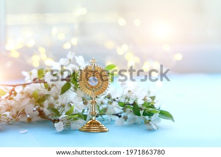 symbol of Catholic Sacrament of Communion and flowers on blurred light background. Eucharist, first communion, Christianity religion, faith in God. Church holiday concept. Golden JHS christogram