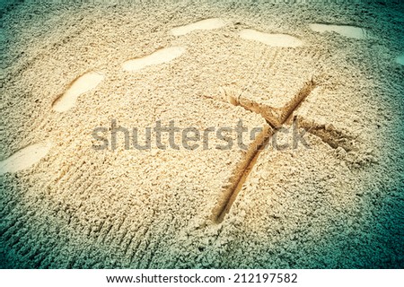 Symbol of the cross drawn in the sand with human footprints passing by