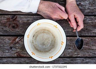 Symbol of financial crisis, poverty and hunger. Senile hands hold an empty old bowl on a wooden background