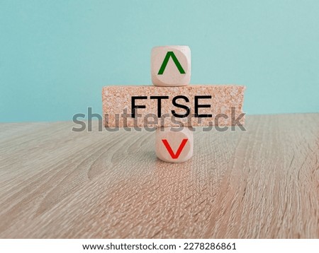 Symbol for the FTSE 100 Index. A brick block with arrow symbolizing that FTSE price are going down or up. Beautiful wooden table blue background. Business and ftse price concept. Copy space. 