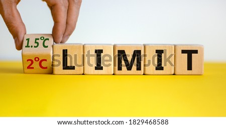 Symbol for limiting global warming. Male hand turns the cube and changes the expression '2 C limit' to '1.5 C limit' or vice versa. Beautiful yellow table white background. Ecological concept. 