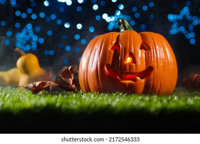 The symbol of the mystical holiday Halloween is an orange pumpkin with a carved face and illuminated by a candle from the inside on green grass against the background of a starry sky.