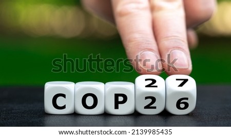 Symbol for the next climate change conference COP27. Hand turns dice and changes the expression COP26 to COP27.