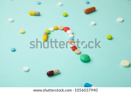 Symbol question mark from colored tablets and capsules on  green background. What medicines to choose better, what will help