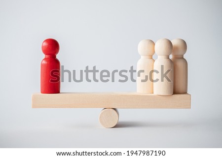 Symbol of scales. Red And Yellow Pawns Figures Balancing On Wooden Seesaw. A wooden plank balancing on a wooden wheel. Concept of harmony and balance. Symbol of work or family, career or relationship
