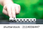 Symbol for a shift from pandemic to endemic. Hand turns dice and changes the German word "Pandemie" (pandemic) to "Endemie" (endemic).