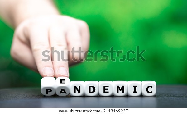 Symbol for a shift from\
pandemic to endemic. Hand turns dice and changes the word pandemic\
to endemic.